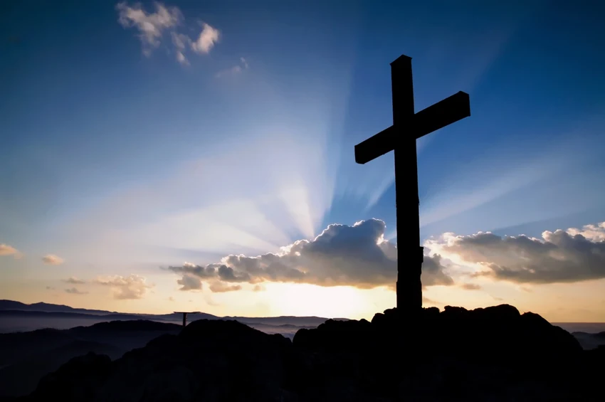 A cross on a hill beneath a sunrise sky